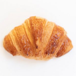 A classic Butter Croissant, featuring layers of flaky, buttery dough that create a light, airy texture and rich flavor.