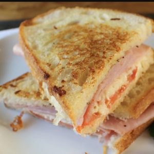 Ham and cheese grilled sandwich with golden, crispy bread and melted cheese oozing between the layers, served on a plate.