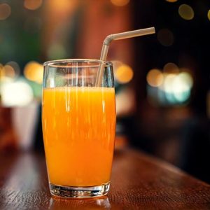 Glass of fresh orange juice with a straw on a wooden table, with a blurred warm-toned background.