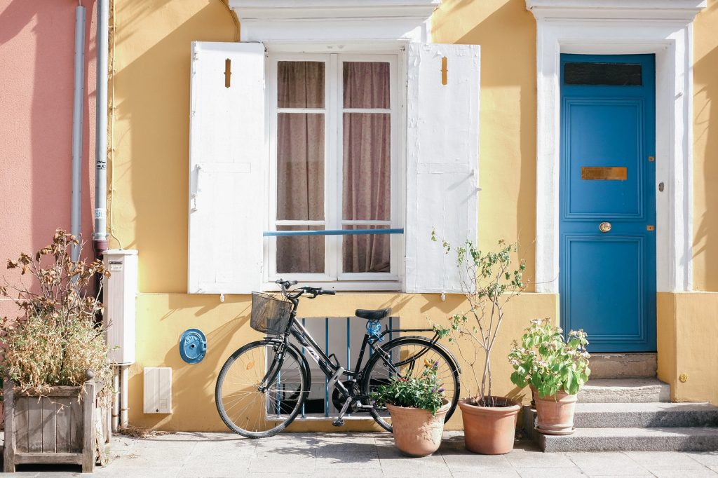 A bike parked outside a yellow building with white windows and bright blue door. 